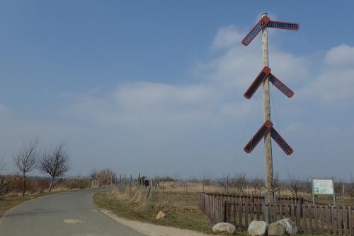 A wooden pole with six red signal arms on top of a hill in the wide open landscape; the sun is shining.