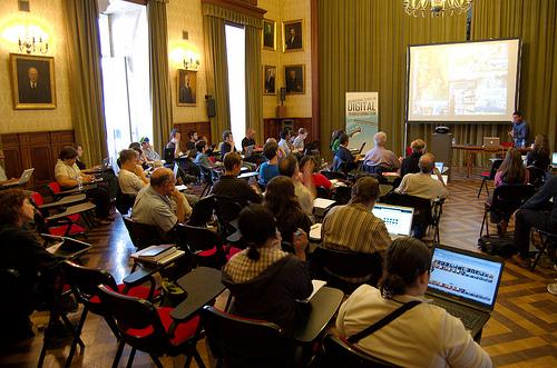 A historic lecture hall, with the audience sitting on chairs, some with laptops.