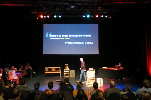Tim on stage, with a quote by Barack Obama projected to the screen: 'There's no sugar coating, the website has been too slow'