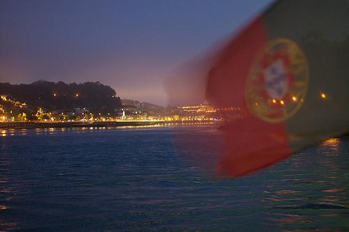 The Portuguese flag blurred from movement in front of the illuminated sky and the city on the shore