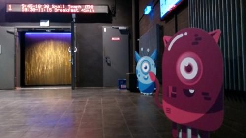 Hallway with door to a theatre, indicating the next talks on a digital display