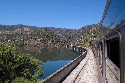 View out of a train window, as the train crosses some water and heads into a hilly landscape