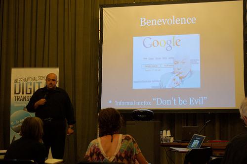 Speaker on stage, with a slide showing a screenshot of Google and Dr. Evil from the Austin Powers movie. Text: 'Benevolence – informal motto: don't be evil'.