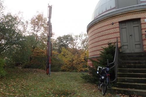 A wooden construction with six red-painted signal arms next to an observatory; a bicycle leans next to it.
